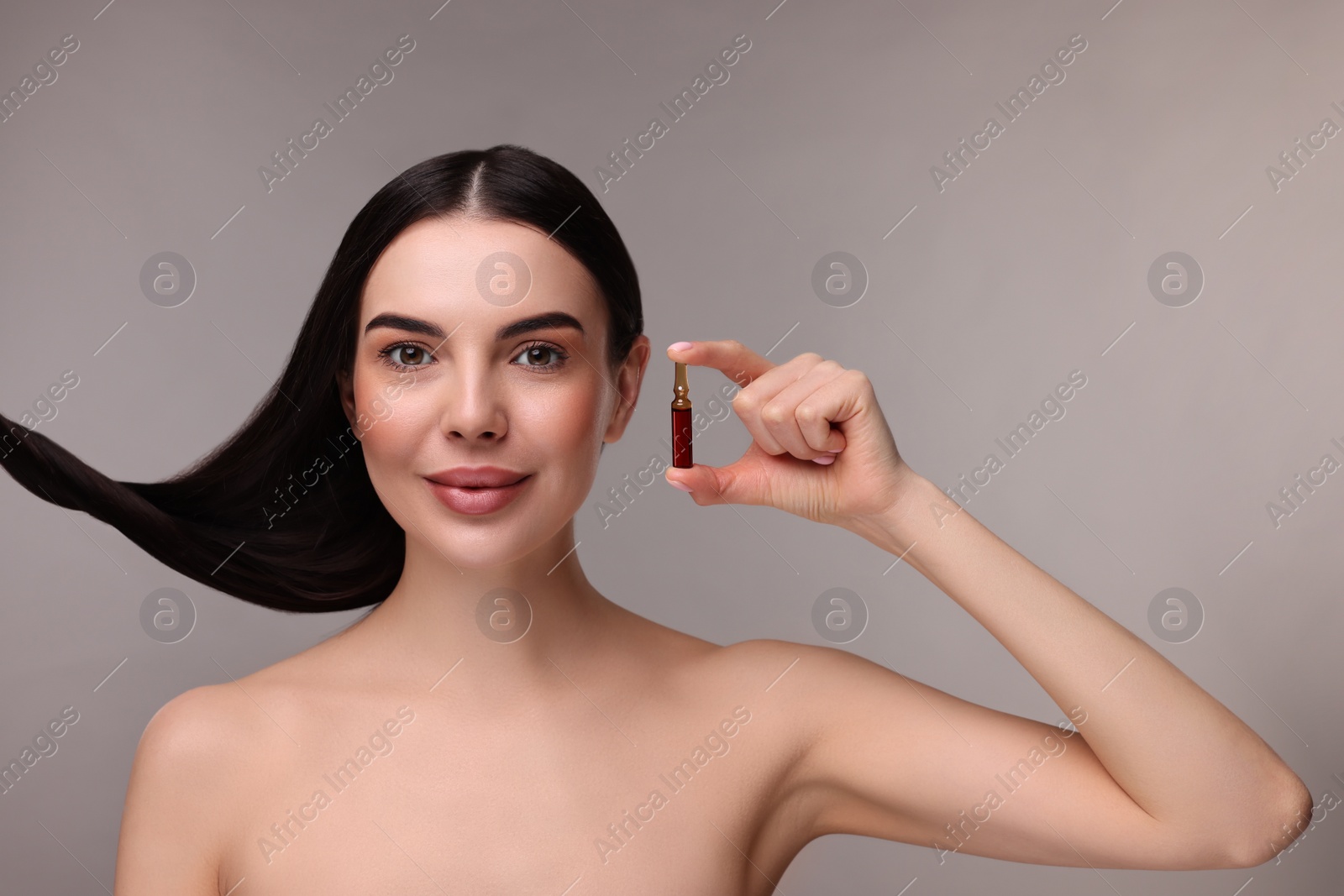 Photo of Beautiful young woman with long healthy hair holding ampoule on grey background