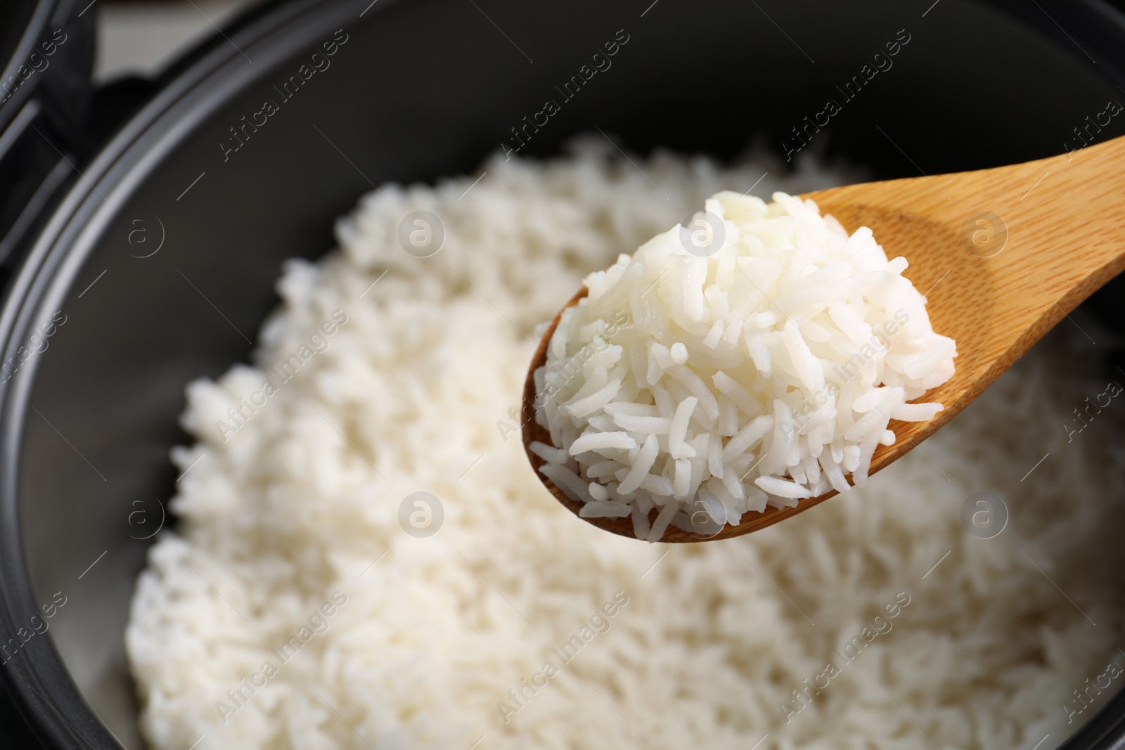 Photo of Spoon with tasty hot rice over cooker, closeup