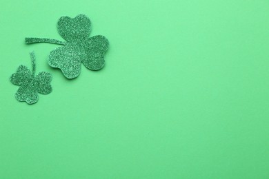 St. Patrick's day. Shiny decorative clover leaves on green background, flat lay. Space for text