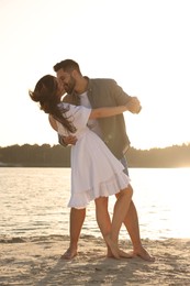 Photo of Happy couple dancing and kissing near river on sunny day