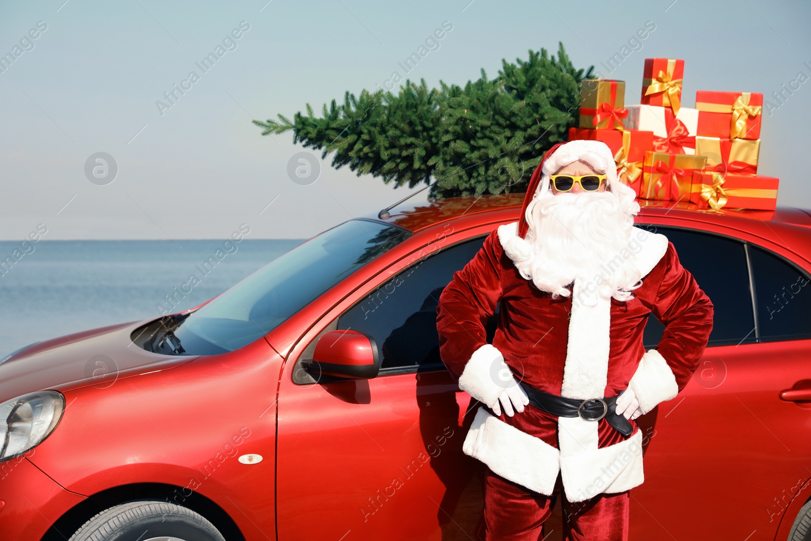 Photo of Authentic Santa Claus near car with presents and fir tree on roof at sea