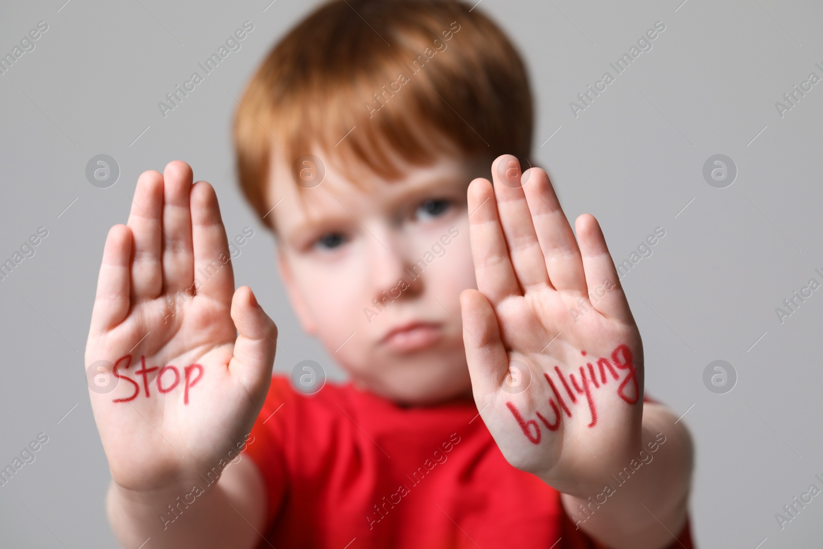 Photo of Boy showing hands with phrase Stop Bullying on light grey background, selective focus