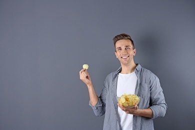 Photo of Man with bowl of potato chips on grey background. Space for text