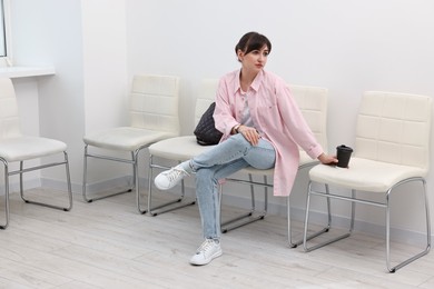 Woman with cup of drink waiting for appointment indoors