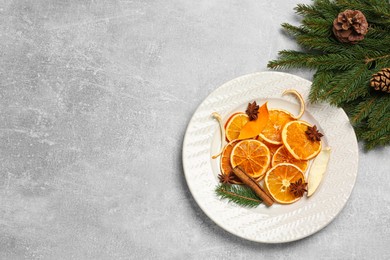 Photo of Flat lay composition with dry orange slices, anise stars, fir branches and cones on light grey table. Space for text
