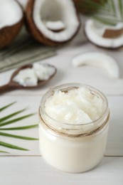 Photo of Jar of organic coconut cooking oil and fresh fruits on white wooden table, closeup