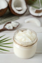 Jar of organic coconut cooking oil and fresh fruits on white wooden table, closeup