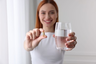 Beautiful young woman with vitamin pill and glass of water, selective focus