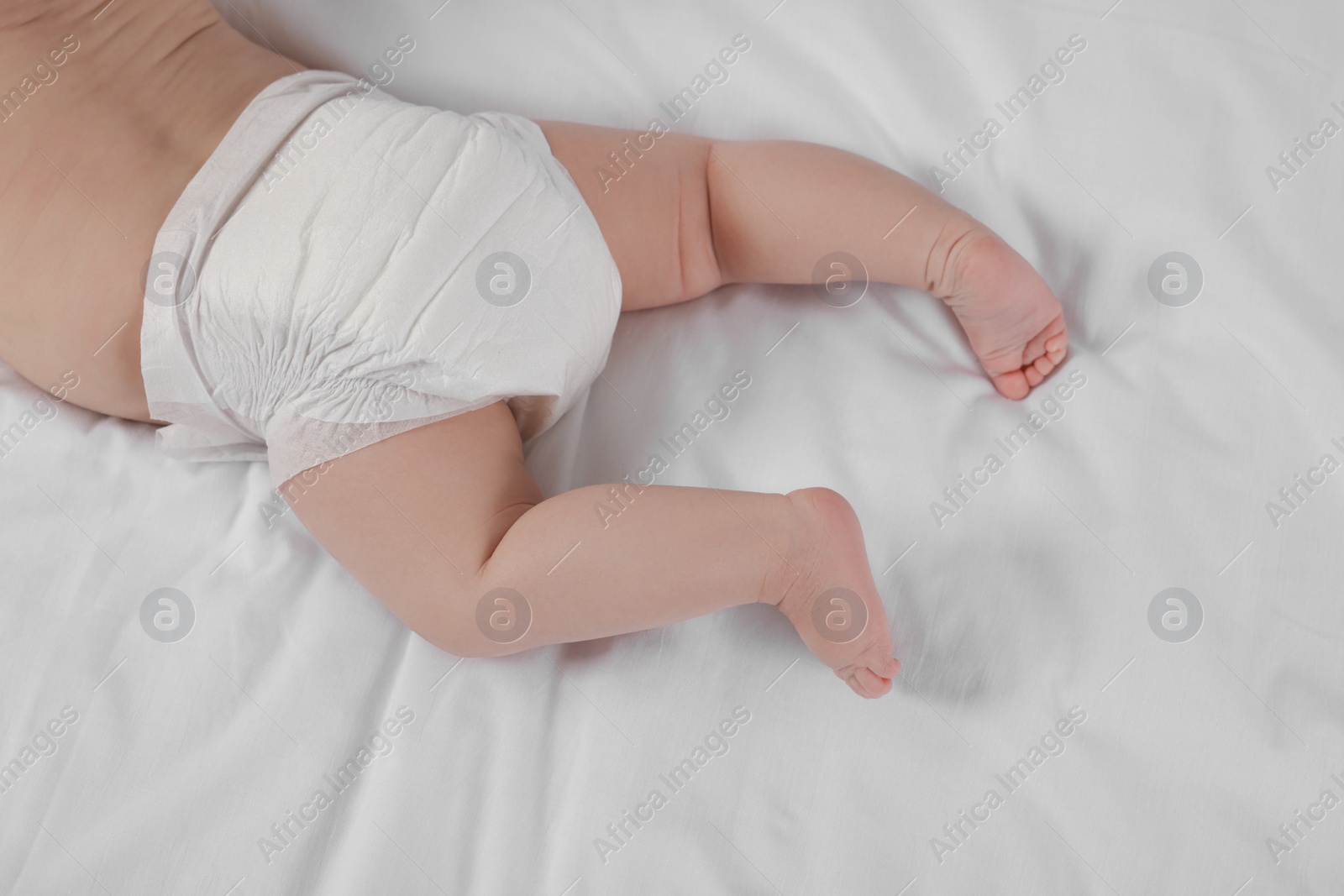 Photo of Little baby in diaper lying on bed, top view