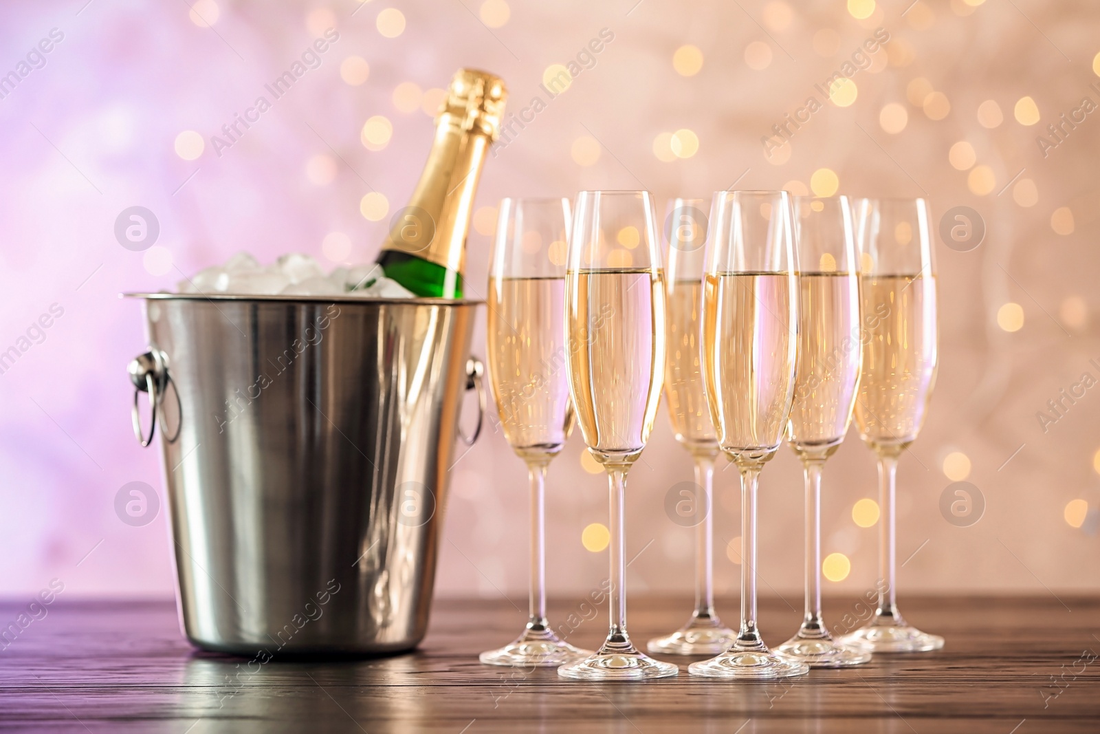 Photo of Glasses with champagne and bottle in bucket on table against blurred lights