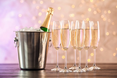 Photo of Glasses with champagne and bottle in bucket on table against blurred lights