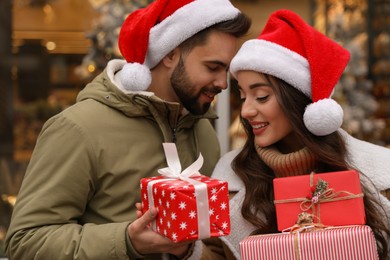 Photo of Lovely couple with Christmas presents near festively decorated store outdoors