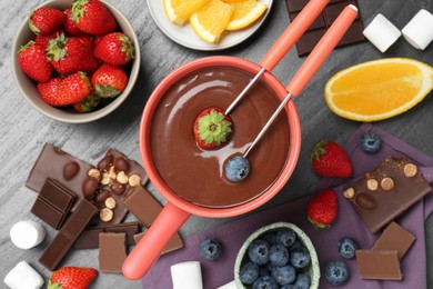 Photo of Fondue pot with melted chocolate, fresh orange, marshmallows and different berries on grey table, flat lay