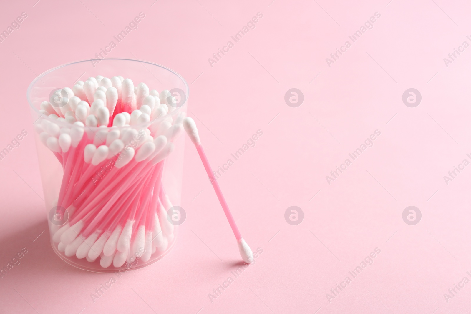 Photo of Plastic container with cotton swabs on color background. Space for text