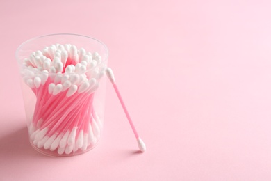 Photo of Plastic container with cotton swabs on color background. Space for text