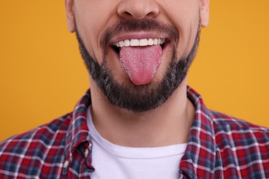 Photo of Happy man showing his tongue on orange background, closeup