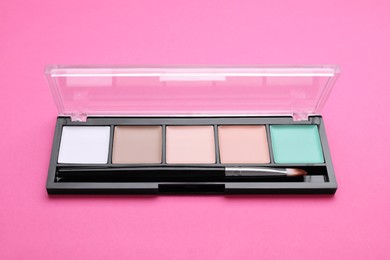 Colorful contouring palette with brush on pink background, closeup. Professional cosmetic product