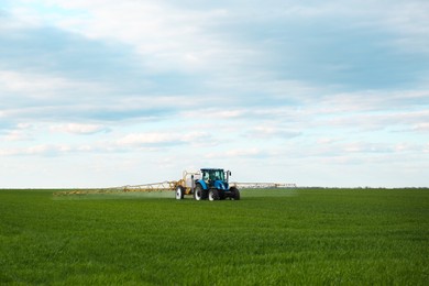 Photo of Tractor spraying pesticide in field on spring day. Agricultural industry