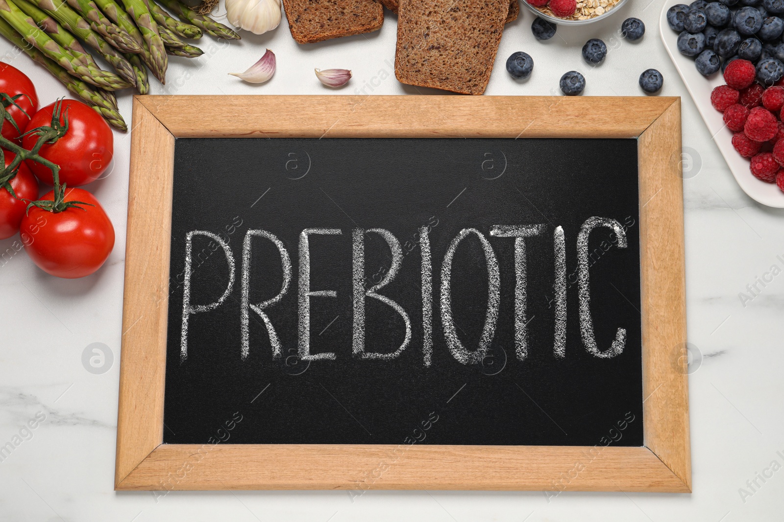 Photo of Blackboard with word Prebiotic and different products on white marble table, flat lay