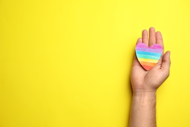 Photo of Man with rainbow heart on yellow background, top view and space for text. Gay symbol