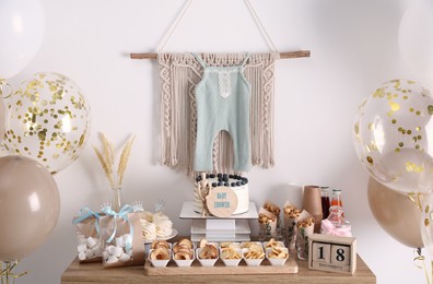 Photo of Baby shower party. Different delicious treats on wooden table and decor near light wall