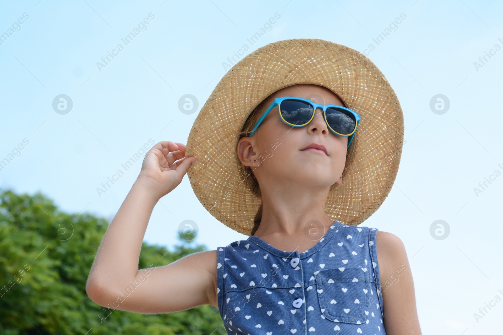 Photo of Little girl wearing sunglasses and hat at beach on sunny day