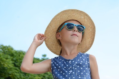 Photo of Little girl wearing sunglasses and hat at beach on sunny day