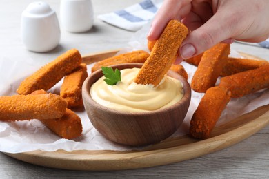 Photo of Woman dipping delicious chicken nuggets into cheese sauce at white wooden table, closeup