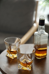 Glasses and bottle of whiskey on table indoors. Space for text