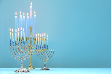 Photo of Hanukkah celebration. Menorahs with burning candles on table against light blue background, space for text