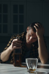 Addicted man with alcoholic drink at table in kitchen