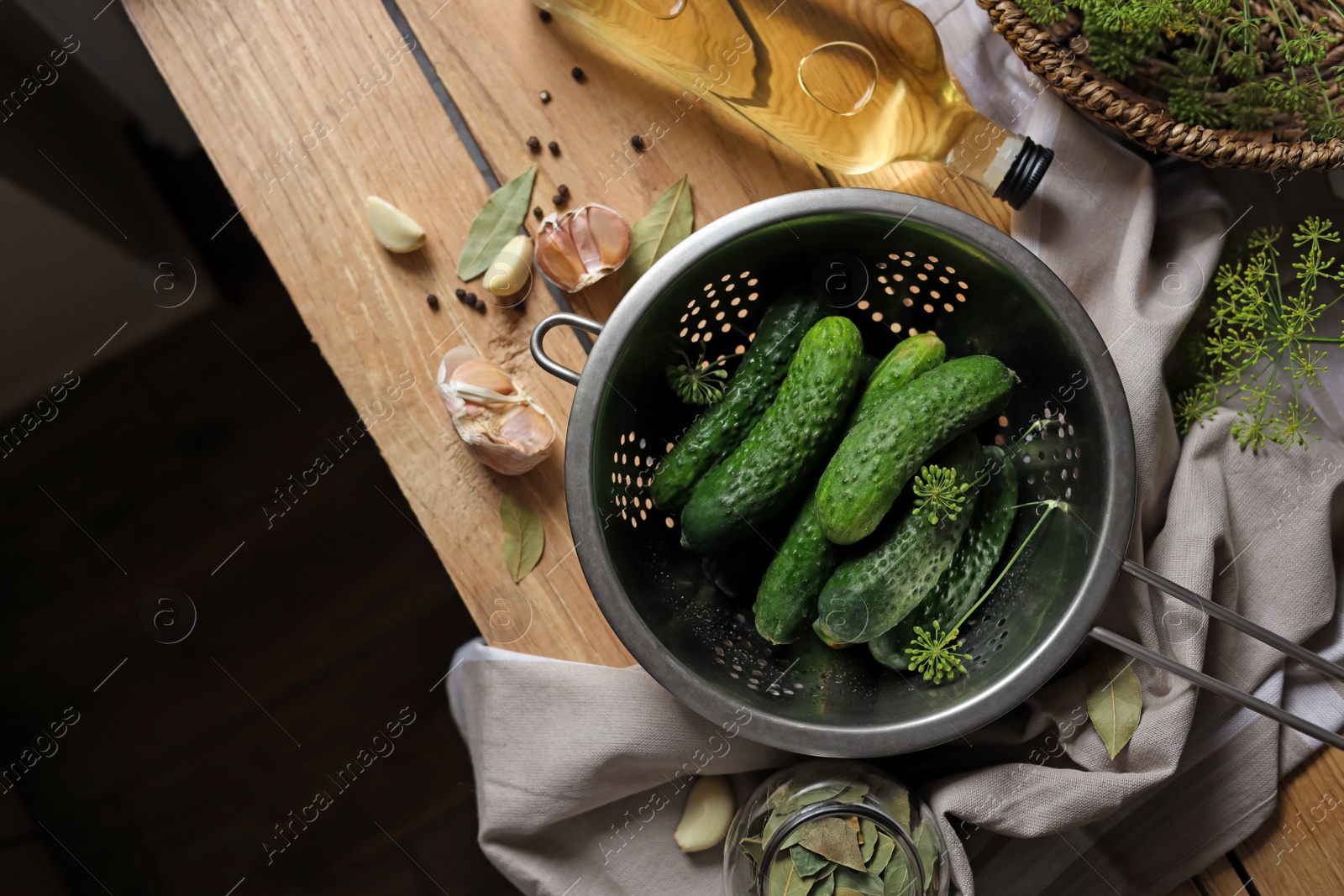 Photo of Fresh cucumbers in colander and other ingredients prepared for canning on wooden table, flat lay. Space for text