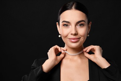 Young woman with elegant pearl jewelry on black background, space for text