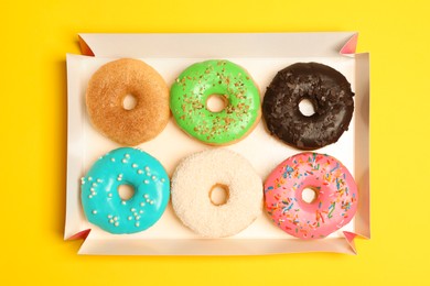 Photo of Box of delicious donuts on yellow background, top view