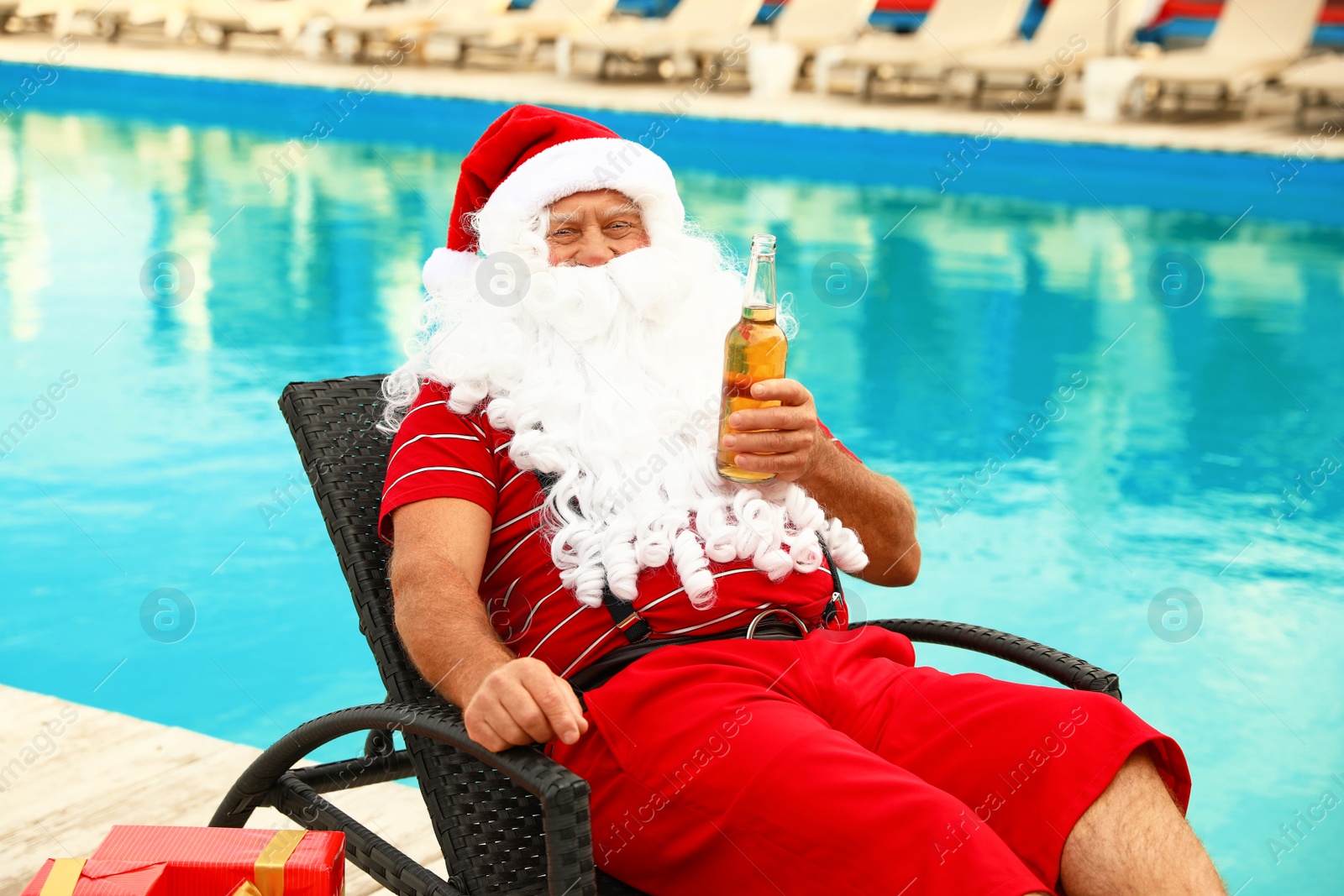 Photo of Authentic Santa Claus with bottle of beer near pool at resort