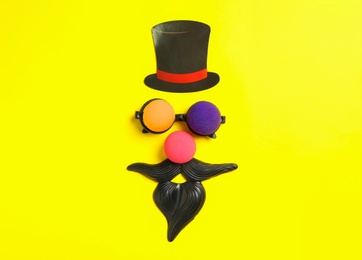 Funny face made with clown's accessories on yellow background, flat lay