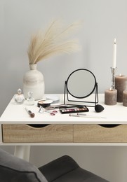 Photo of Dressing table with mirror, cosmetic products, perfumes and burning candles in makeup room
