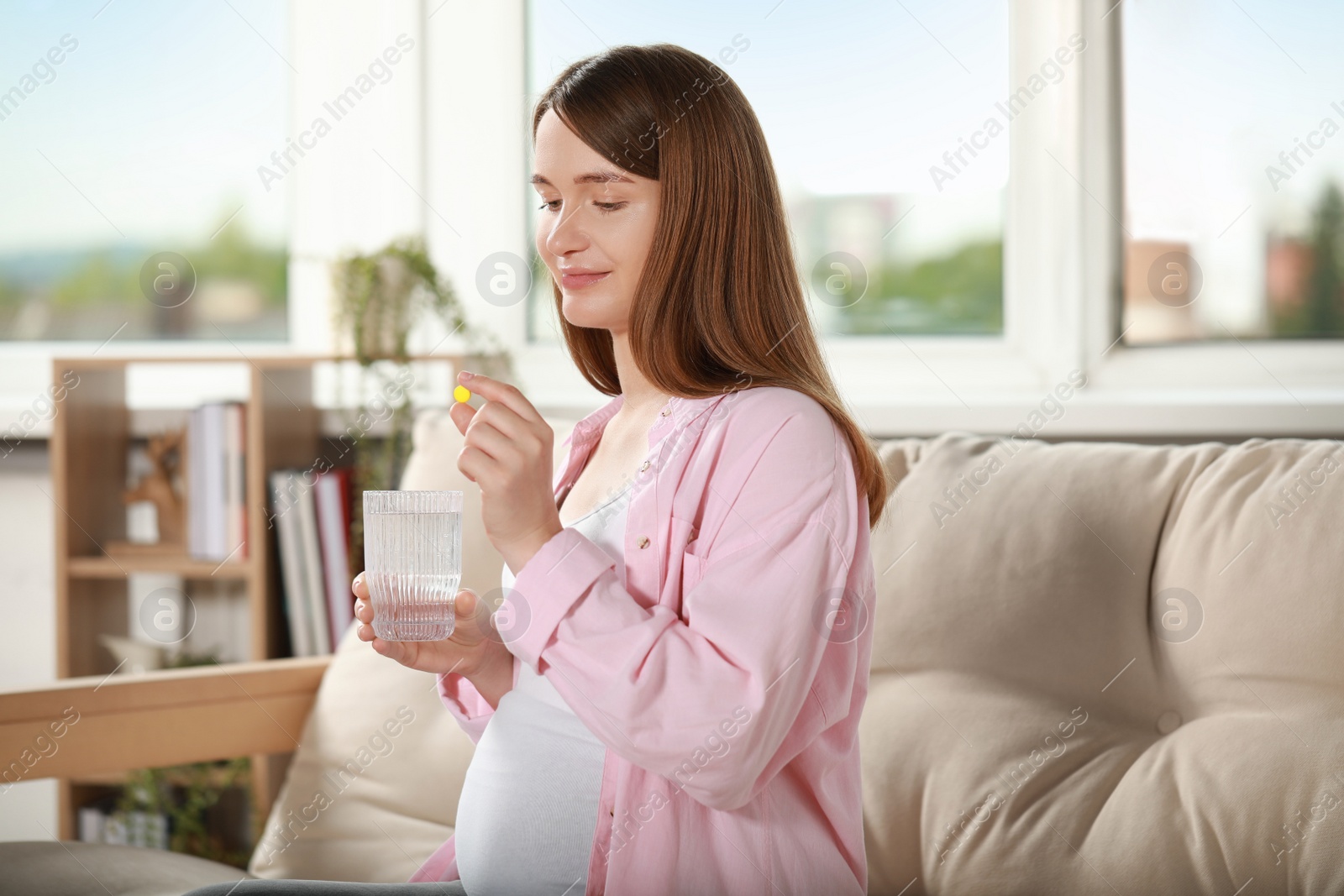 Photo of Beautiful pregnant woman holding pill and glass of water at home