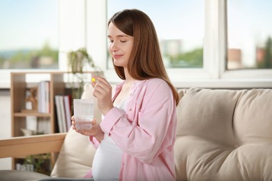 Photo of Beautiful pregnant woman holding pill and glass of water at home