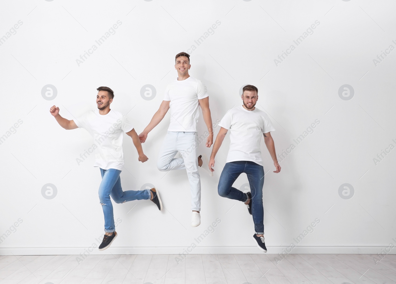 Photo of Group of young men in jeans jumping near light wall