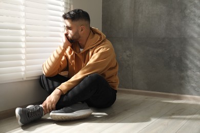 Photo of Sad man sitting on floor near window. Space for text