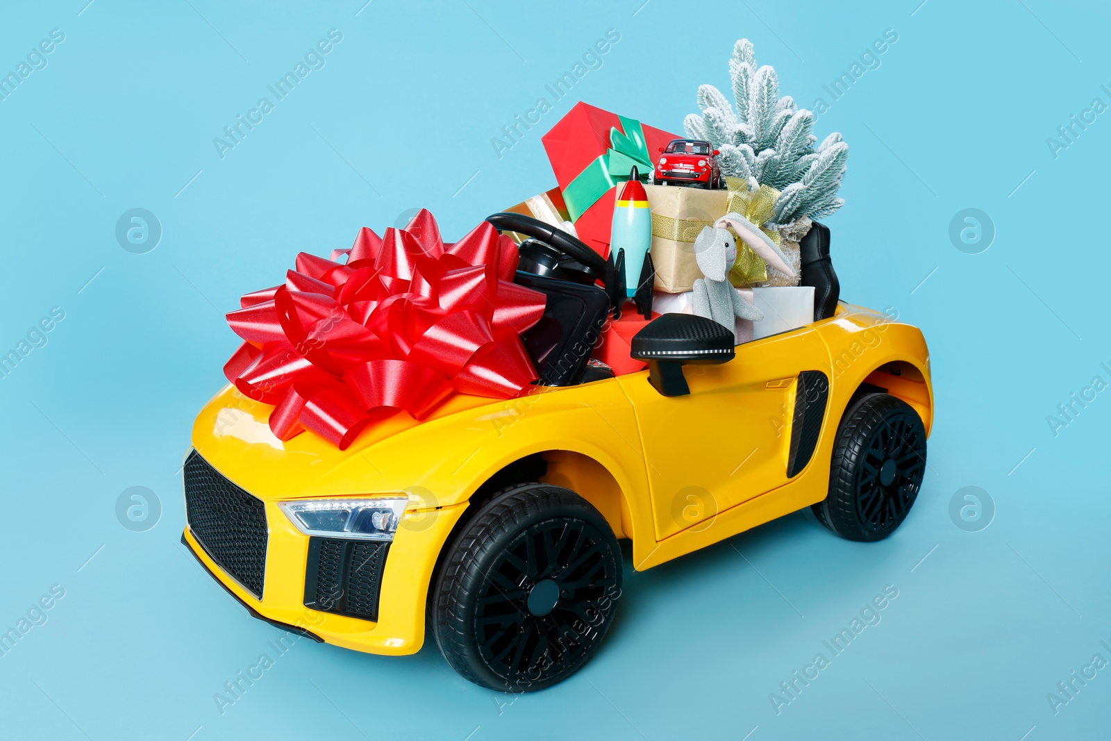 Photo of Child's electric car with toys, gift boxes and Christmas decor on light blue background