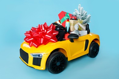 Photo of Child's electric car with toys, gift boxes and Christmas decor on light blue background