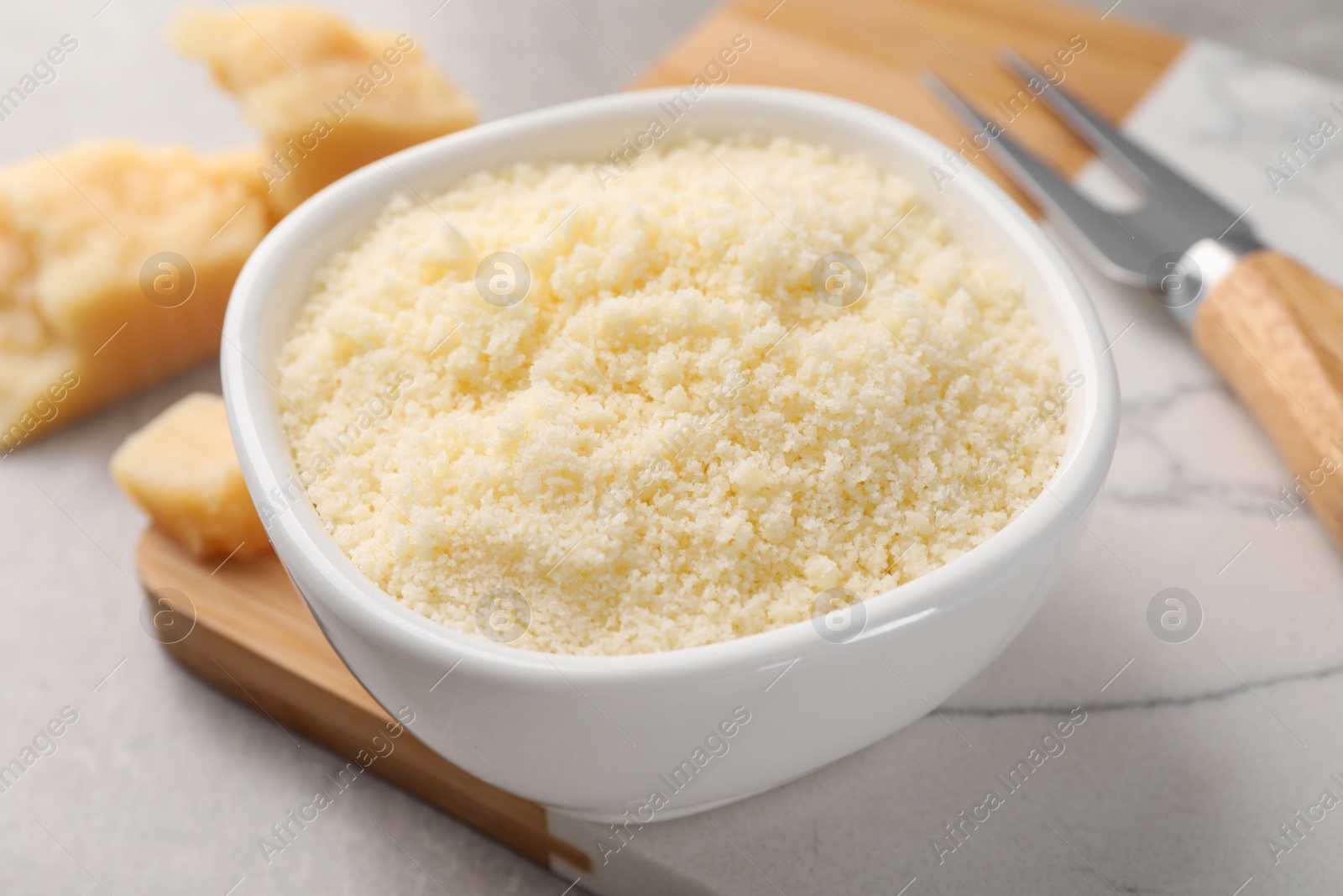 Photo of Bowl with grated parmesan cheese on light table, closeup