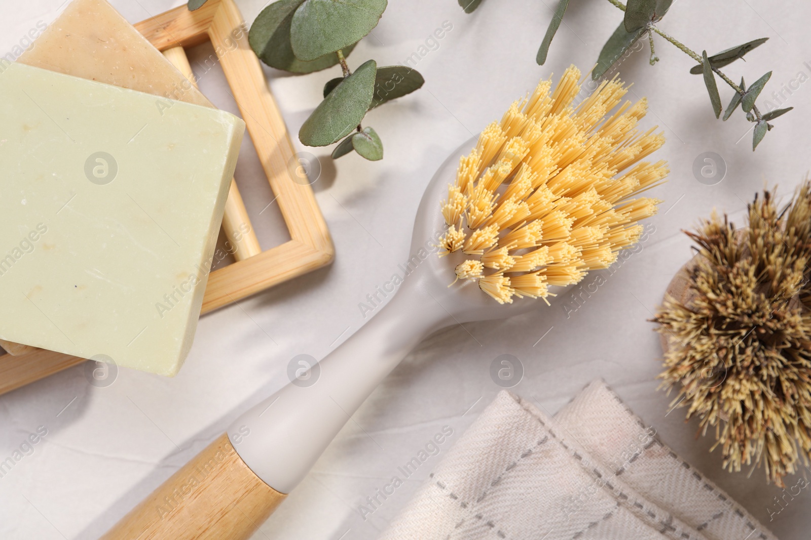 Photo of Cleaning brushes, soap bars and eucalyptus leaves on white table, flat lay