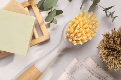 Cleaning brushes, soap bars and eucalyptus leaves on white table, flat lay