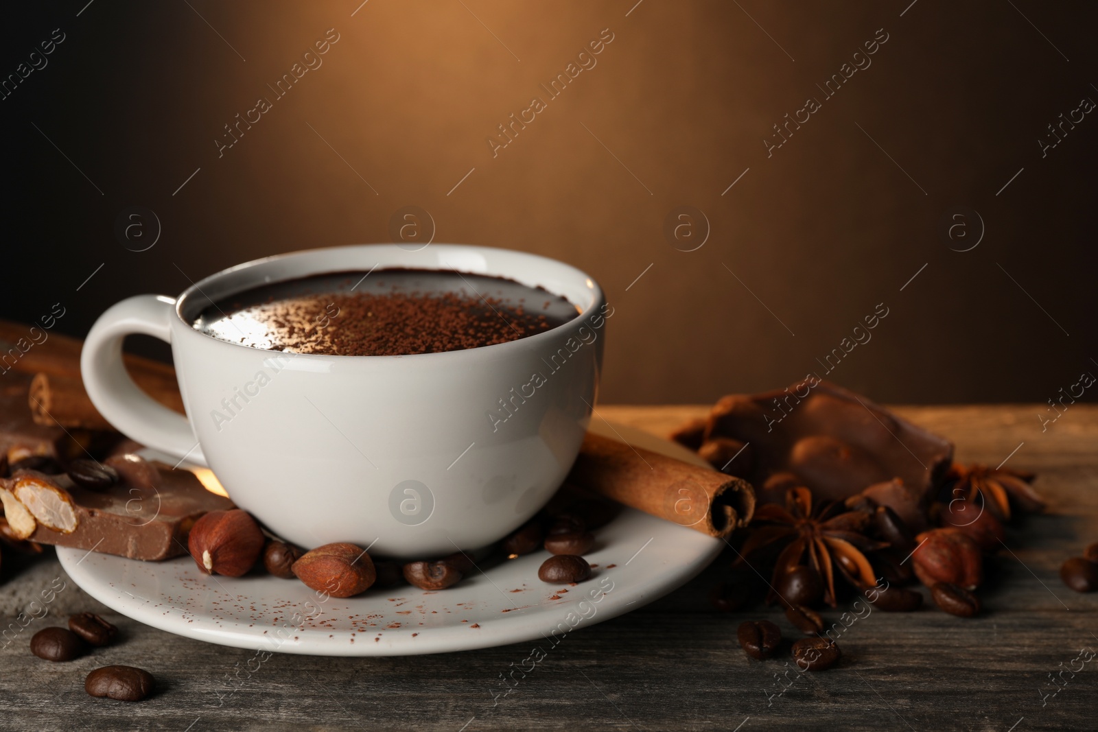 Photo of Cup of delicious hot chocolate, spices and coffee beans on wooden table. Space for text