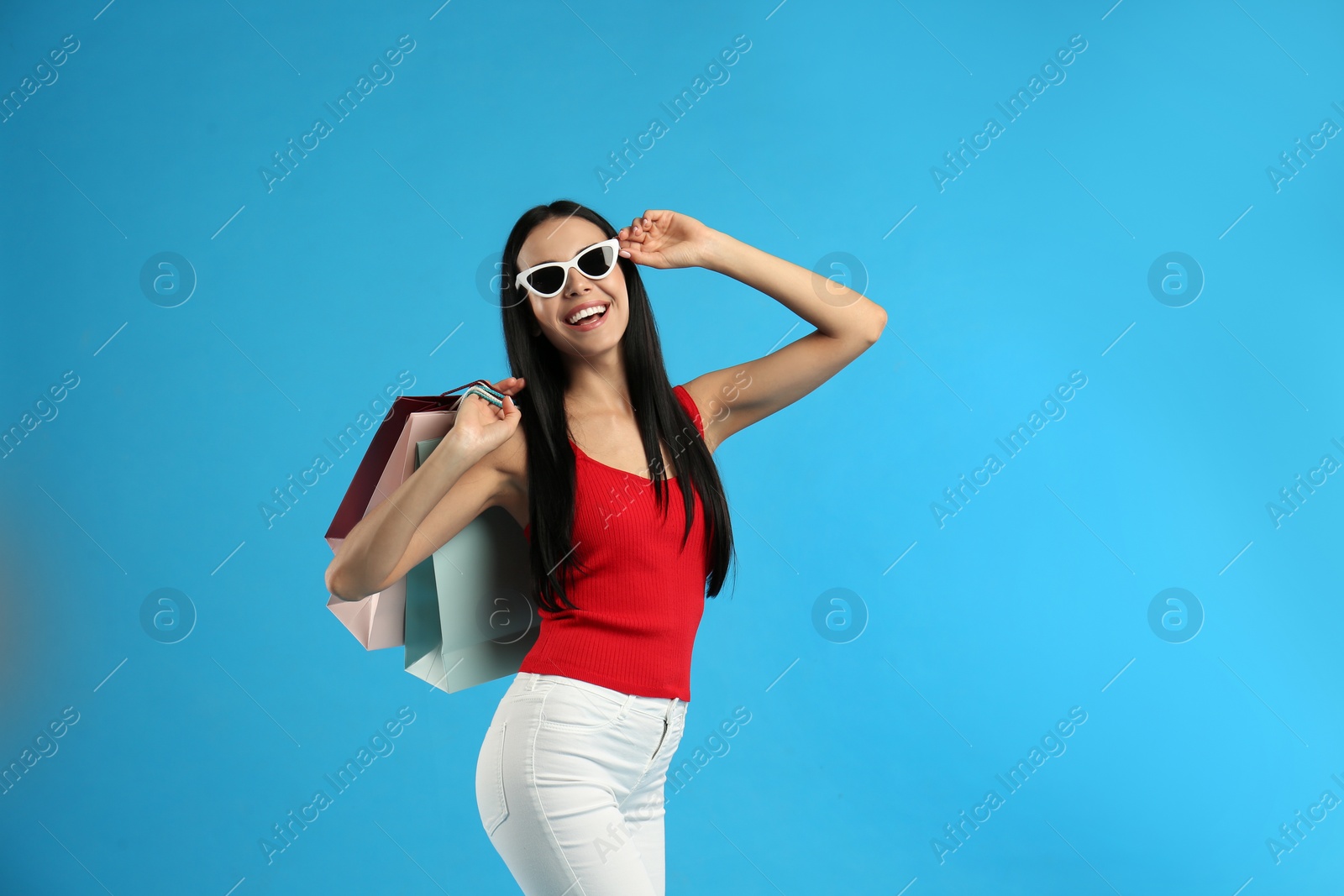 Photo of Beautiful young woman with paper shopping bags on light blue background