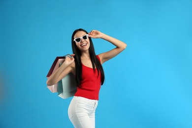 Beautiful young woman with paper shopping bags on light blue background