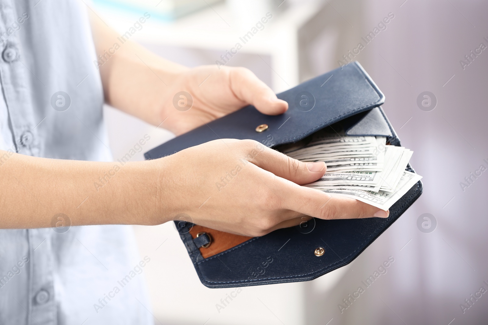 Photo of Woman putting money into wallet on blurred background, closeup